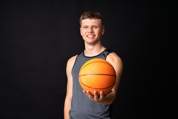 Handsome young man playing basketball over isolated black wall
