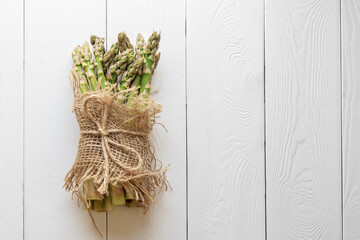 Asparagus shoots are tied with a jute rope on white boards. Fresh asparagus is wrapped with a jute cloth on a white wooden background with a copy of space.