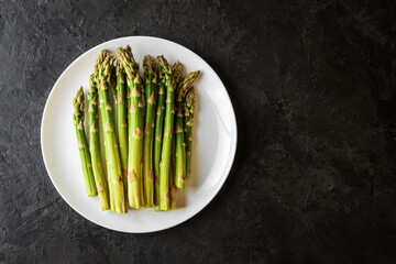 Asparagus shoots on a white plate.Plate of fresh asparagus on a black concrete background with a copy of space.
