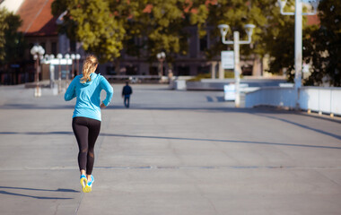 Back of a young female jogger running through an empty town