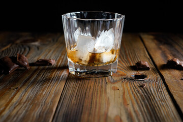 malt scotch whiskey with ice and chocolate on wooden table