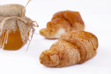 croissant with crispy crust and honey in a jar with burlap, on a white plate,