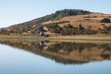 reflection of trees and golden hill in the lake