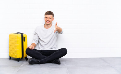 Young handsome man sitting on the floor with a suitcase handshaking after good deal
