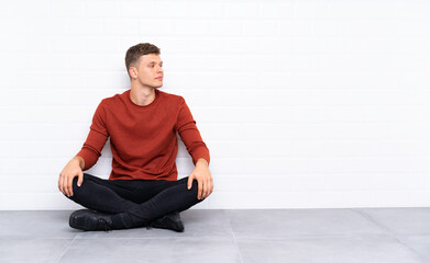 Fototapeta premium Young handsome man sitting on the floor looking to the side