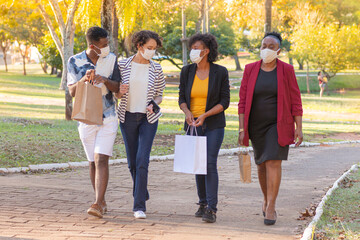 Family members strolling in city park with shopping bags.