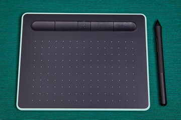 Graphic tablet with pen stylus on green background.