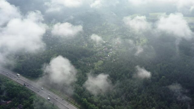 Flyby of a drone through the clouds. Over fluffy Low morning clouds over a large freeway running through the forest. 
