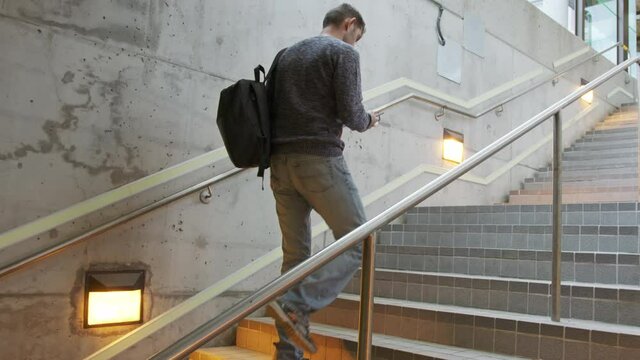 High quality 4k video of a young man who climbs the stairs at the station and holds a phone in his hands and a backpack on his back. A man hurries on a train, bus, airplane subway, transport