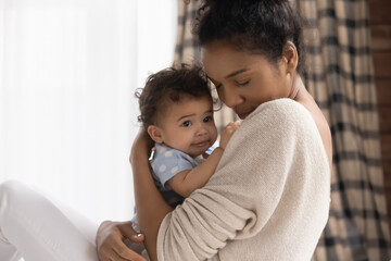 Close up loving African American young mother holding adorable toddler daughter, cuddling, family...