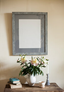 vintage interior,still life on the table against wall with bouquet of peonies, books,and candlestick and the frame for the photo or picture