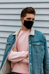 Good-looking young man in denim blue stylish jacket in pink sweatshirt in black protective mask...