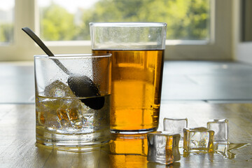 Red and black tea and lemonade in a transparent glass with ice on a background of a sunny window.