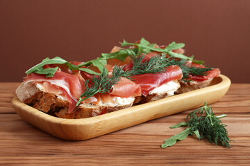 Buckwheat toasts with goat cheese, ham and arugula lying on a bamboo plate on a wooden table.