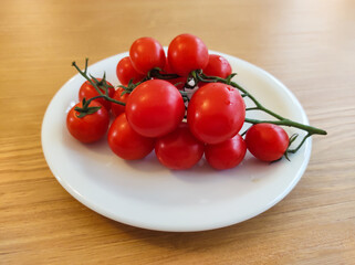 Closeup of white plate with bunch of mini tomatoes on wooden table.