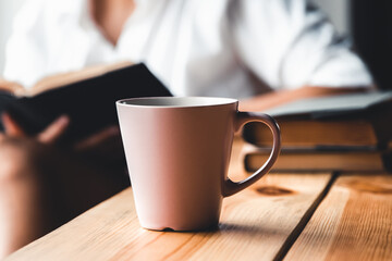 Woman in the morning drinks coffee and reads old book in a white shirt. Education, drink. manicure
