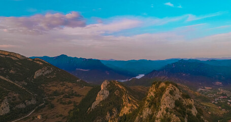 Obraz premium Landscape of several mountains with trees and a small lake in between and the blue sky with some clouds.