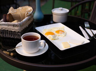Two fried eggs, a cup of tea and cheese slices on the black table