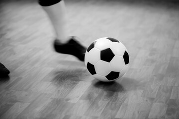 Fototapeta na wymiar Black and white image of Futsal ball with motion blurry futsal player run and contol ball to shoot to goal on wooden floor in sports hall. Youth futsal league. Soccer game indoor.
