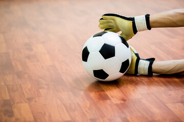 Ball in hand of futsal goalkeeper on wooden futsal floor. Indoor soccer sports hall. Football...
