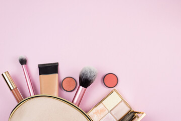 Overhead view of make up products spilling out of a pink cosmetics bag on to a pink background. beauty, fashion and shopping concept