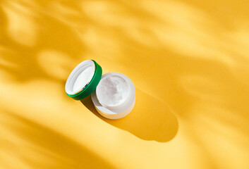 Bottle of cosmetic, coconut oil, on a yellow background. Place for text. Hard shadows. Flat lay. Copy space. background with tropical plant shadow