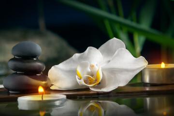 Obraz na płótnie Canvas Black zen stones,candles and white orchids on a wooden plank on the surface of the water. SPA, relaxation, meditation concept