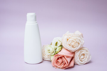 Obraz na płótnie Canvas Moisturizing body lotion in a white tube next to a rose flower on a pink background. Copy space