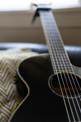 Fototapeta premium Acoustic guitar resting on black leather sofa by the living room window. natural light. 