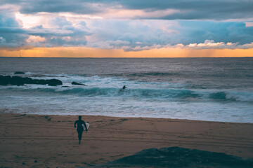 Obraz premium Silhoette of surfer at sunrise, running down to the beach with his surfboard to get some waves