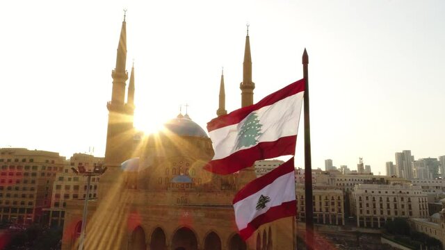 Beirut, Lebanon 2019: sunset lift up drone shot on Lebanese flag with mosque, church and sun flaring on the side in the background a shot symbolizing resistance and unity during the revolution