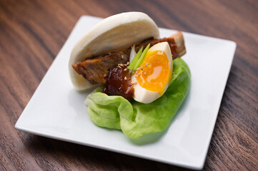 roasted pork bun with soft boiled egg on a white plate