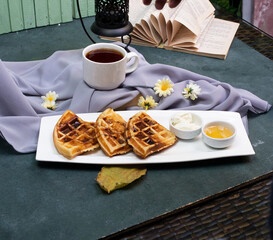 Waffles sliced and served with caramel sauce and a cup of tea on the blue table