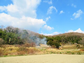 日本の田舎の風景　2月　早春の畑焼き　山の木々と青空