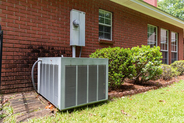 Old style air conditioner unit next to home, brick and bushes with clean yard.