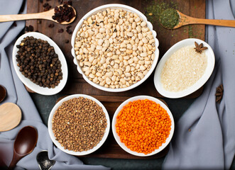 Obraz na płótnie Canvas Red lentils, wheat, rice and buckwheat in a white bowl on a wooden board, top view