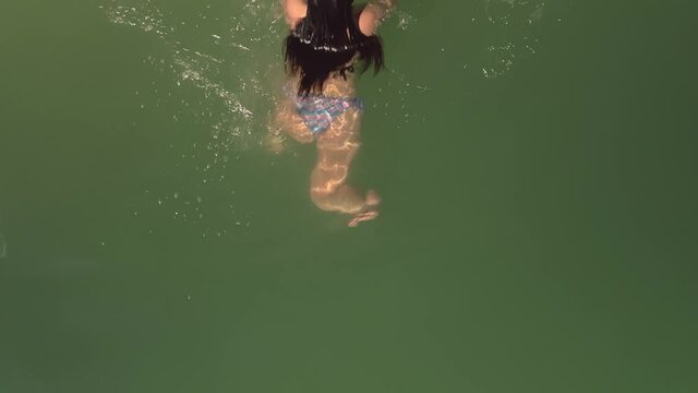 Aerial shot above female in bikini swimwear blowing kiss and swimming in beautiful green water surface