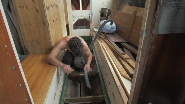 Young man hoovering bilge of wooden boat interior