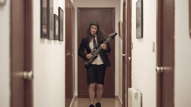 Young man in suit plays toy guitar and dances in apartment hallway