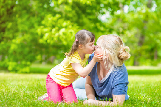 Little girl with special needs kisses her mother in a summer park. Empty space for text