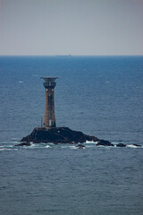 Close up image of a lighthouse on top of a little rock in the middle of the sea. The stone tower is away from the coast and lonely. Vastness of ocean is dramatic as it blends into the horizon.