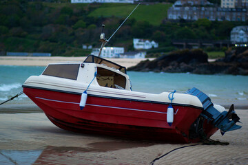 Close up image of a small red and white motor fishing boat that is stranded on shore at low tide. Image was taken at sunset with green hills, sea and buildings in the background.