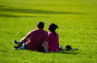 A couple is sitting side by side on the grass of a park with their shoes off. They are leaning back in a relax position to enjoy the beautiful atmosphere in this sunny spring day.
