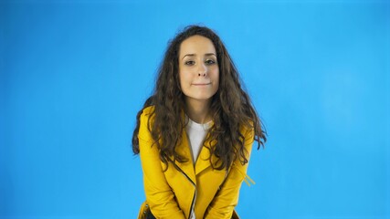 Fototapeta premium Happy Pretty Woman in yellow jacket Winking Eye in Studio with blue Background.