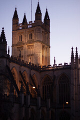 Naklejka premium Close up image of the tower of the historic Bath Abbey against clear night sky. Artificial lights illuminate the tower and give it a warm look.