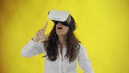 Happy young woman with virtual reality headset or 3d glasses on yellow background at studio.