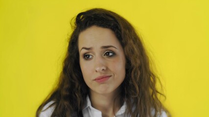 Young beautiful disappointed woman posing on camera on yellow background.