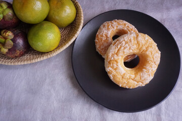 Donuts on a black ceramic plate with the tangerine and mangosteen in a beautiful Thai wicker. Alternative food concept. The background is a white cloth with copy space in Thailand.