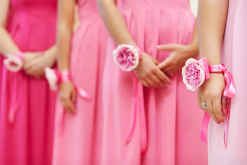 Hands of bridesmaids with peony flowers bracelet in pink dresses