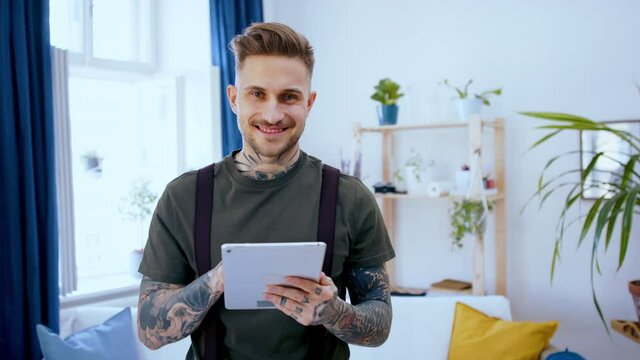 Man with tablet standing indoors at desk in home office, using tablet.